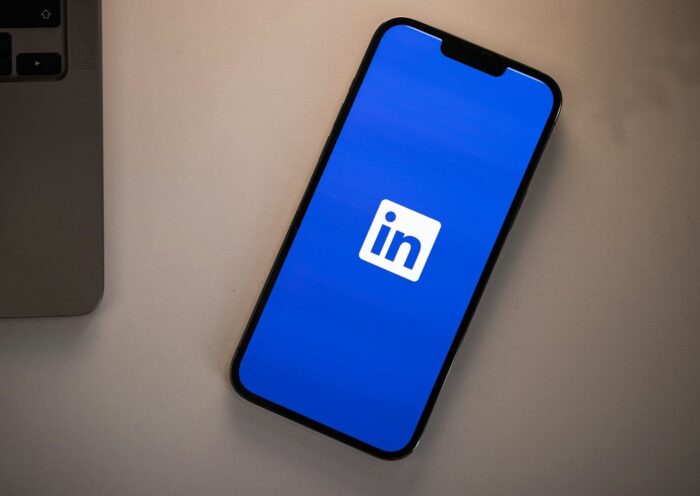 A smartphone displaying the LinkedIn logo on a bright blue screen on a desk