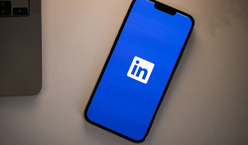 A smartphone displaying the LinkedIn logo on a bright blue screen on a desk