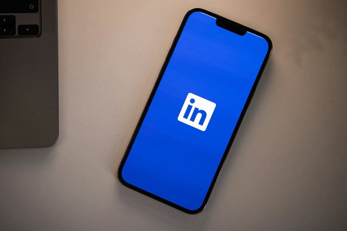 A smartphone displaying the LinkedIn logo on a bright blue screen on a desk